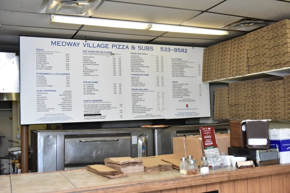 The menu board above the counter, with stacks of pizza boxes beside it
