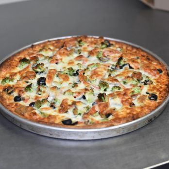 A broccoli and black olive pizza on a metal pan, topped right to the edge
