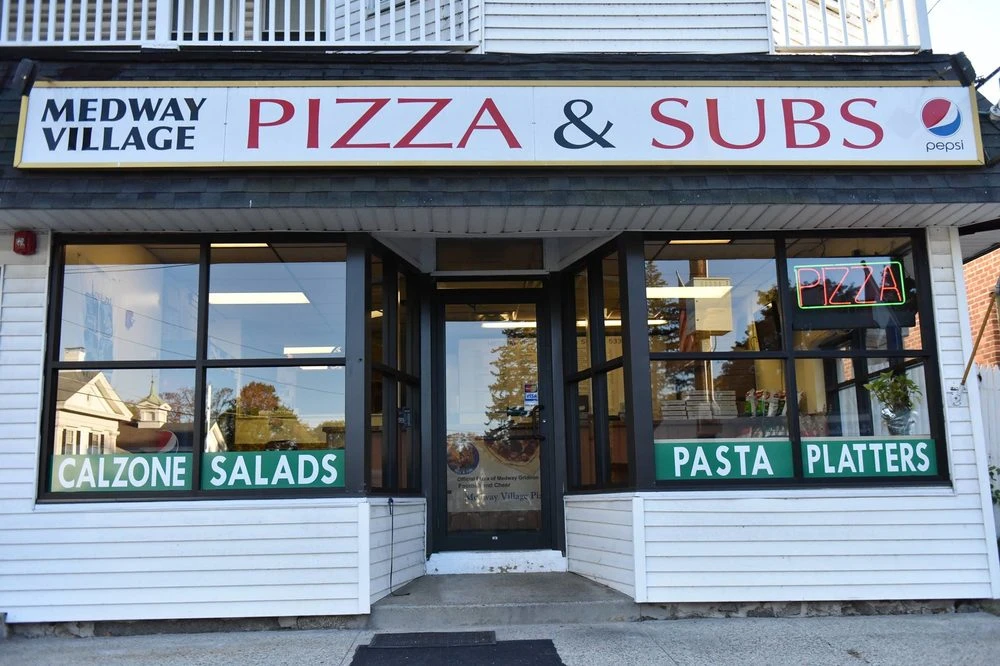 The storefront of Medway Village Pizza & Subs on Village Street in daylight